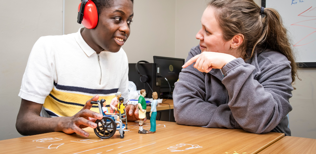 a student and a tutor practicing communication and social skills while using small human figures in different situations to help illustrate certain statements or contexts